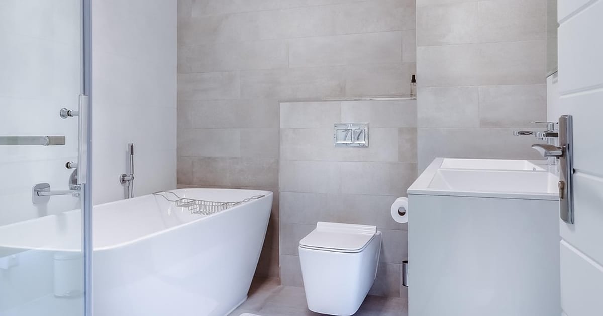Helles Badezimmer mit Glasduschwand, frei stehender Badewanne, Wand-WC und grauen Fliesen